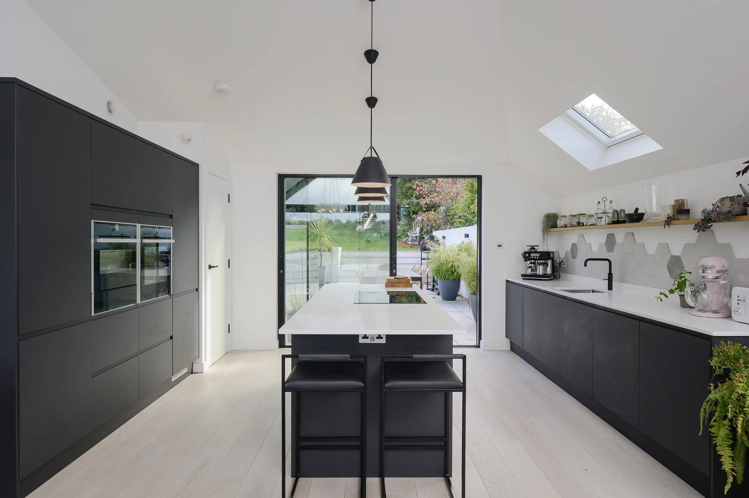 Dark kitchen with a white-topped island, rooflight over the units beyond, garden doors open, upside down house, Haslemere