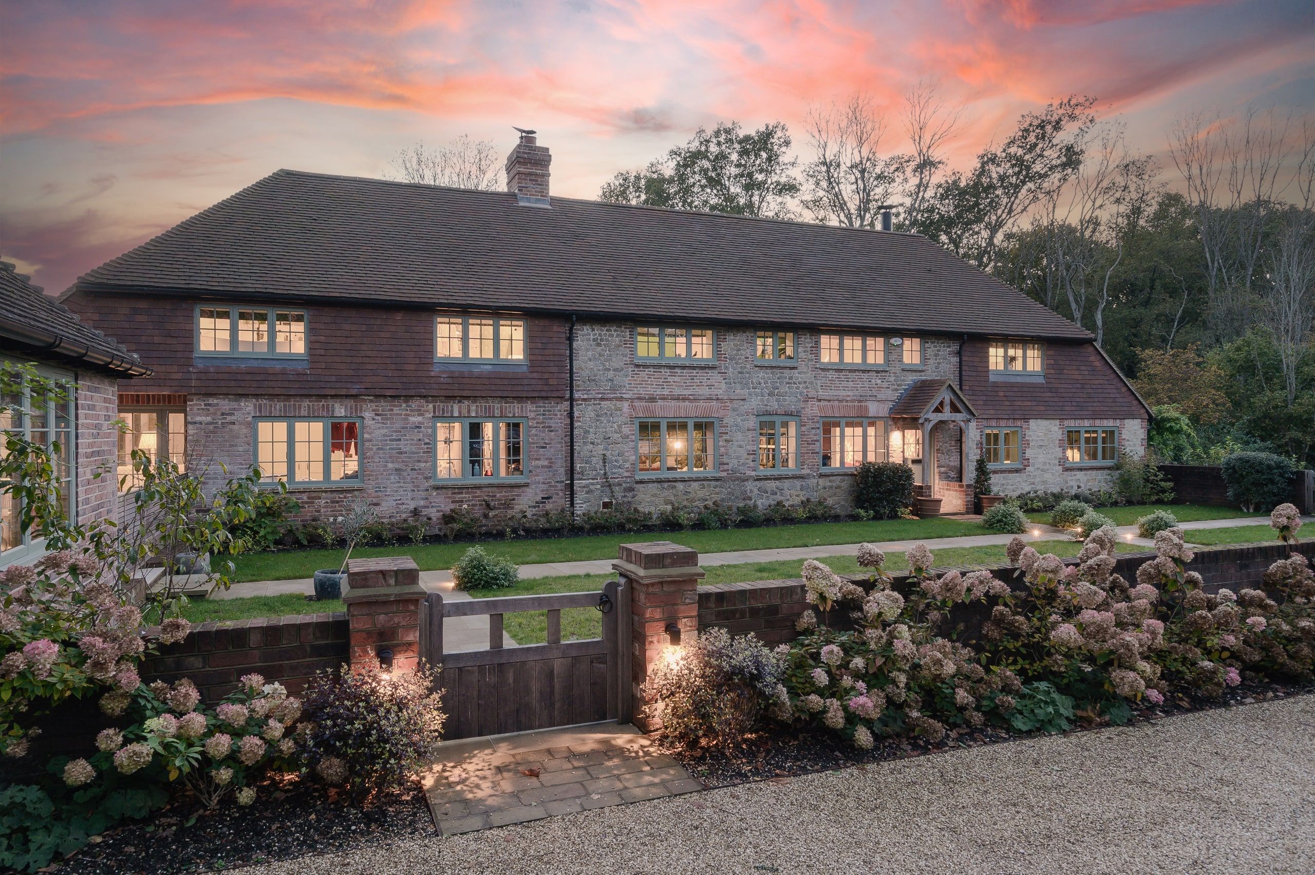 Front elevation at dusk, with the oak porch, gate and hydrangeas along the gravel drive, country house, Lodsworth