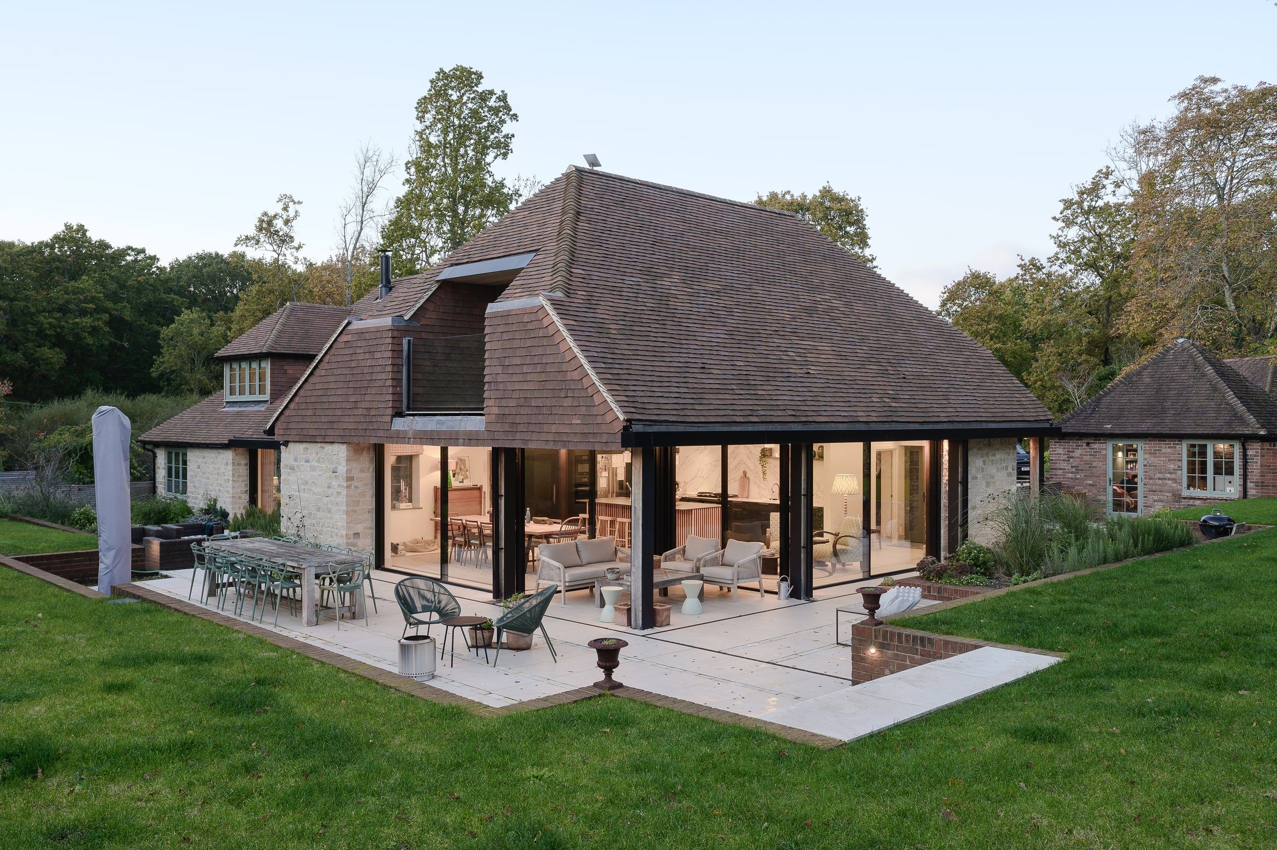 The house at dusk with the loggia and kitchen lit from within, seen across the lawn, country house, Lodsworth