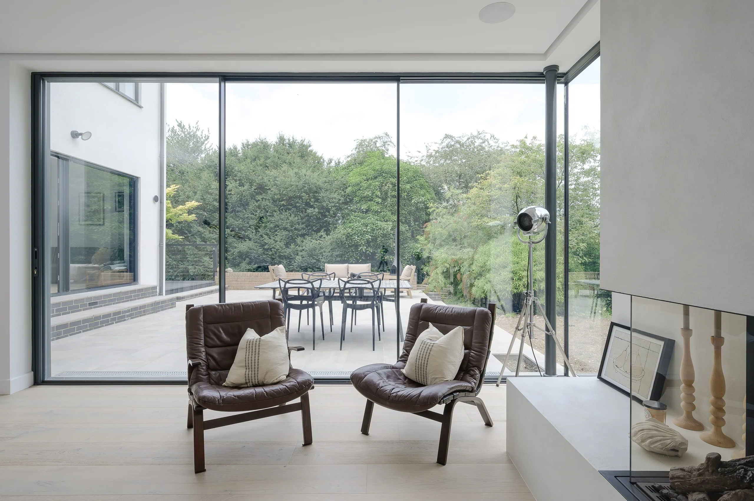 Leather chairs by full-height glazing in the living room, looking out to the terrace, 1960s house, Haslemere