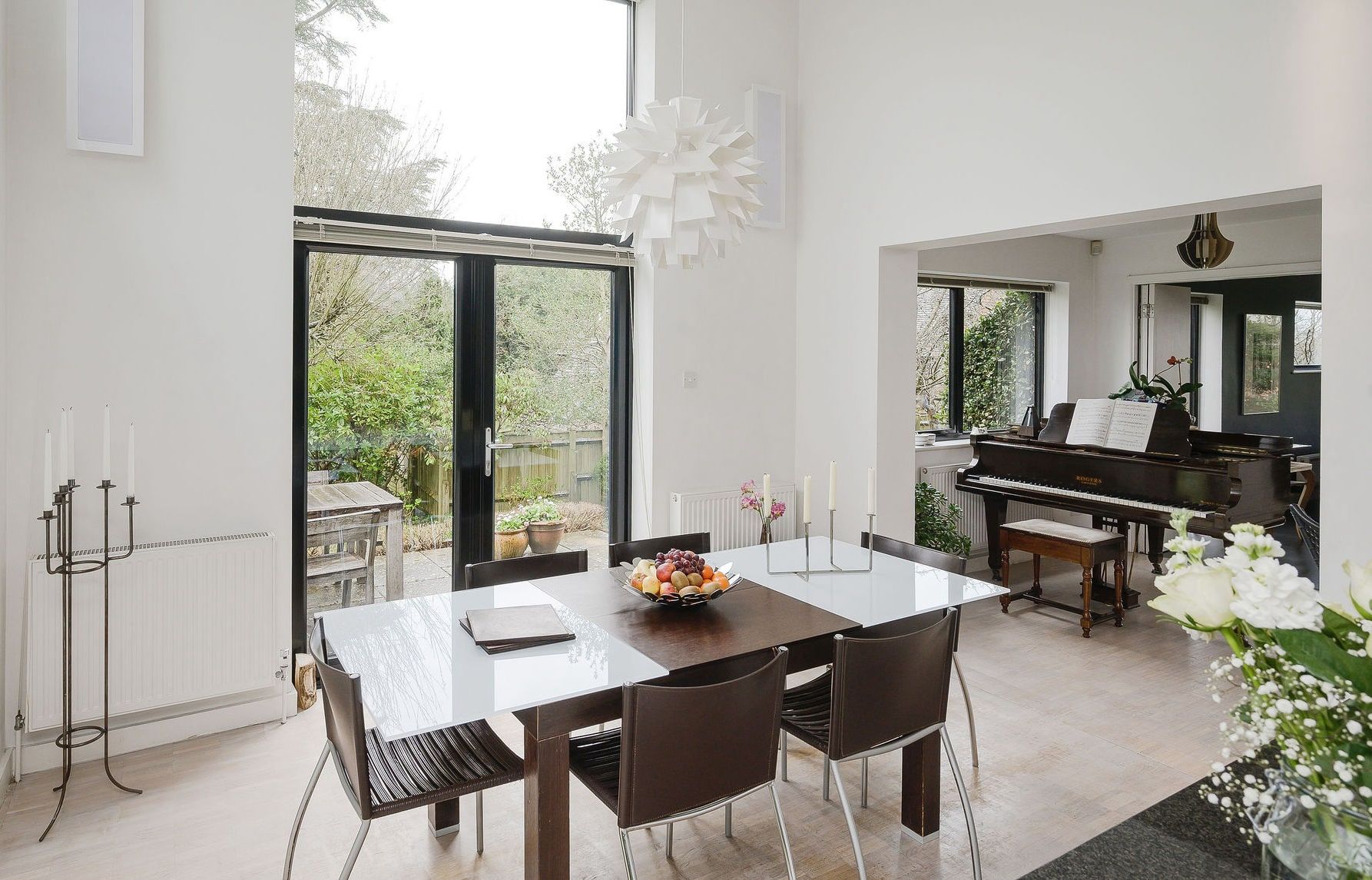 Dining table beside full-height glazed doors with the piano room beyond, 1960s house, Fernhurst.