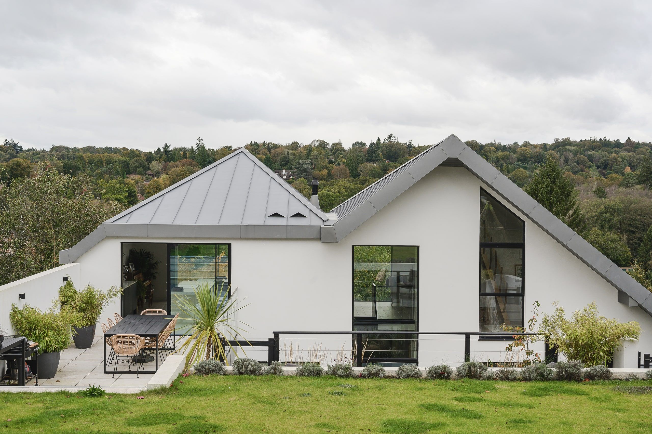 White rendered house with twin zinc roofs sweeping to the ground, seen across the lawn, upside down house, Haslemere