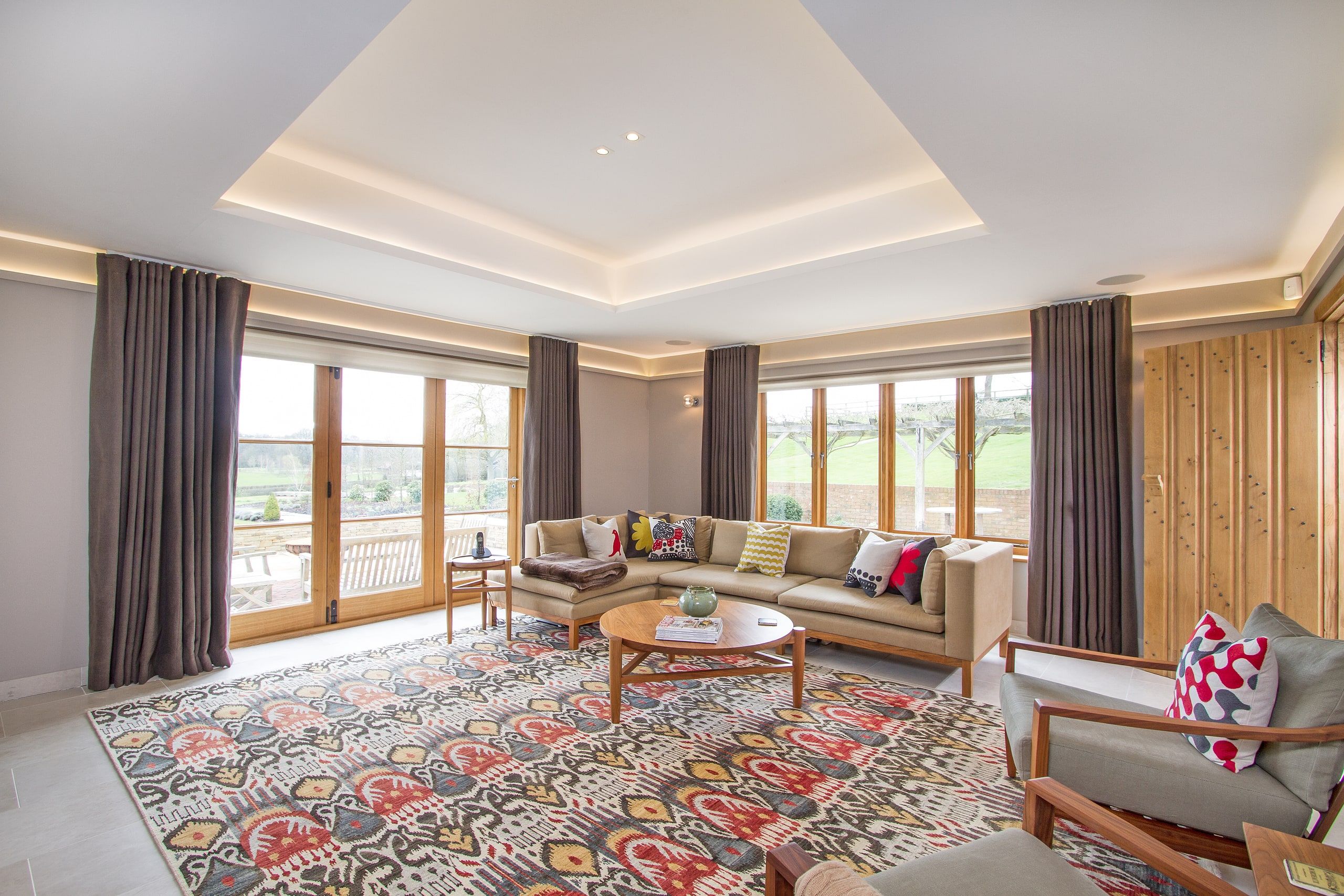 Sitting room with a cove-lit recessed ceiling and full-height windows to the grounds, listed country house, Chiddingfold.