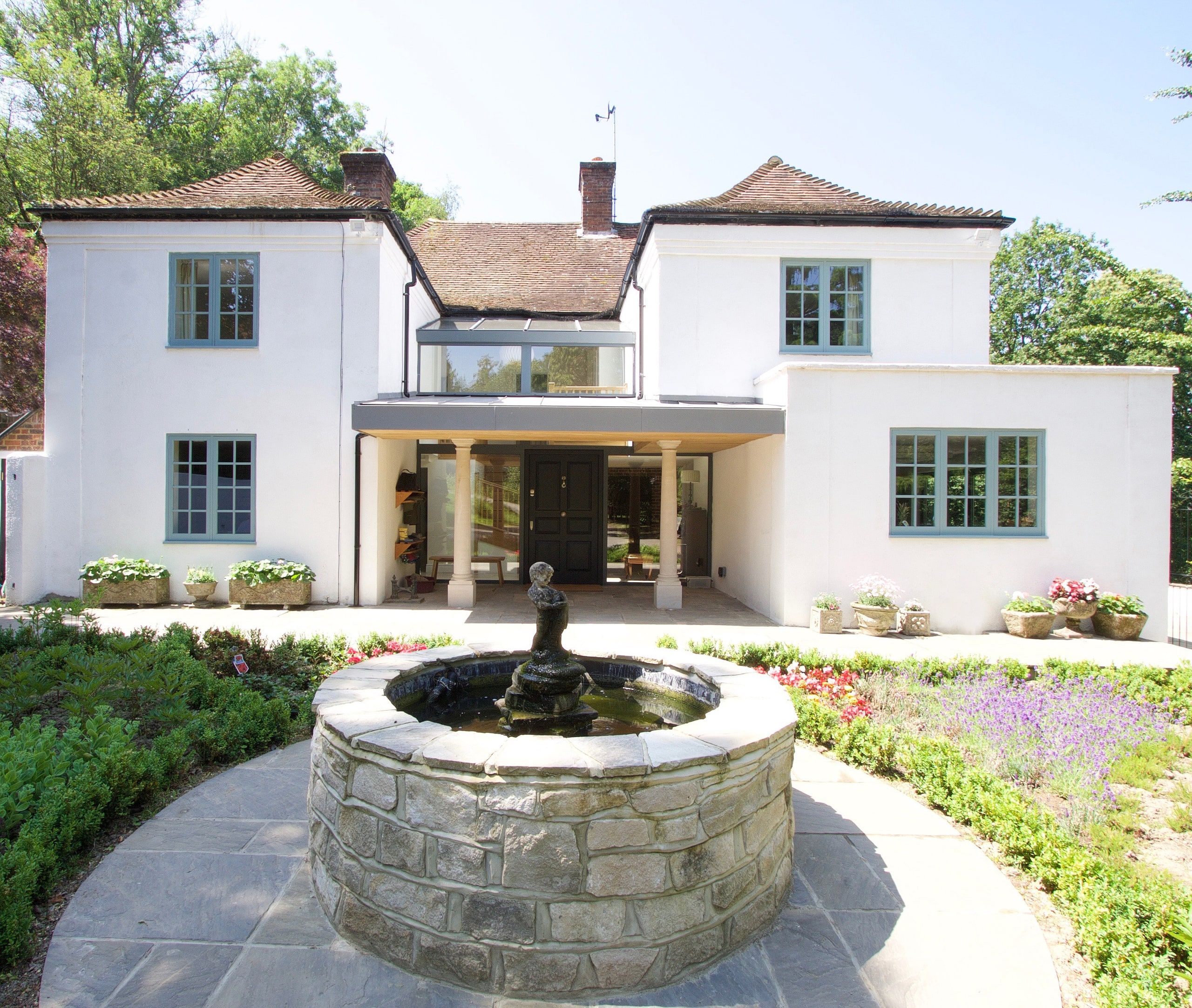 Circular stone fountain in the planted forecourt below the recessed porch, 1930s country house, Mole Valley.