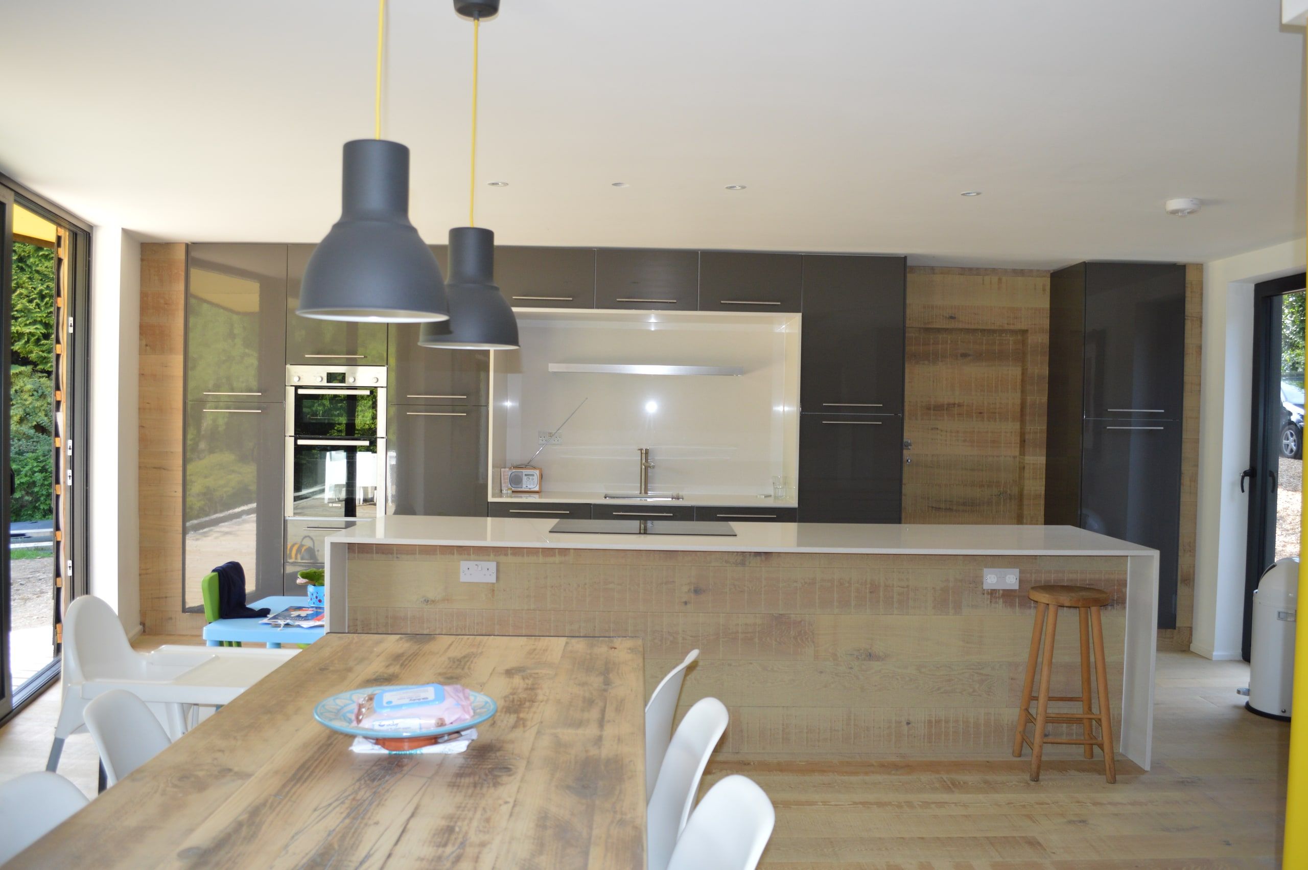 Open-plan kitchen and dining room with an oak table under grey pendant lights, 1960s house, Haslemere.