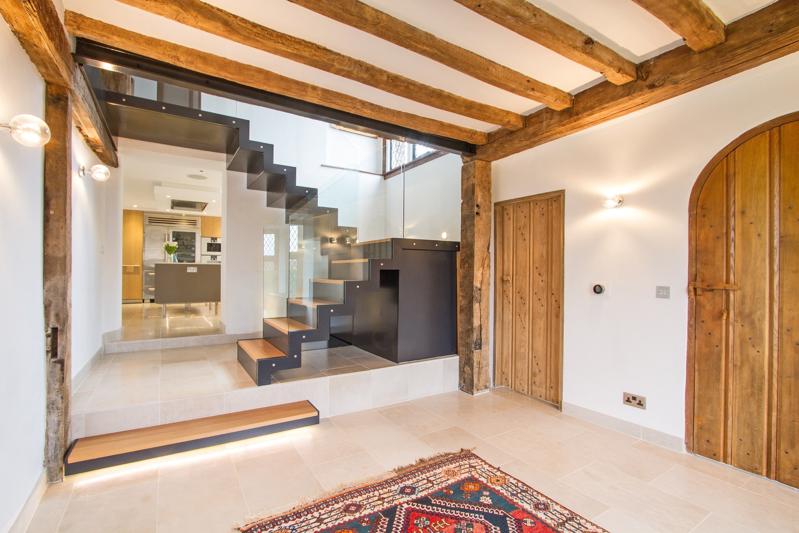 Feature staircase seen past 17th-century oak beams and an arched plank door, Grade II listed country house, Chiddingfold.
