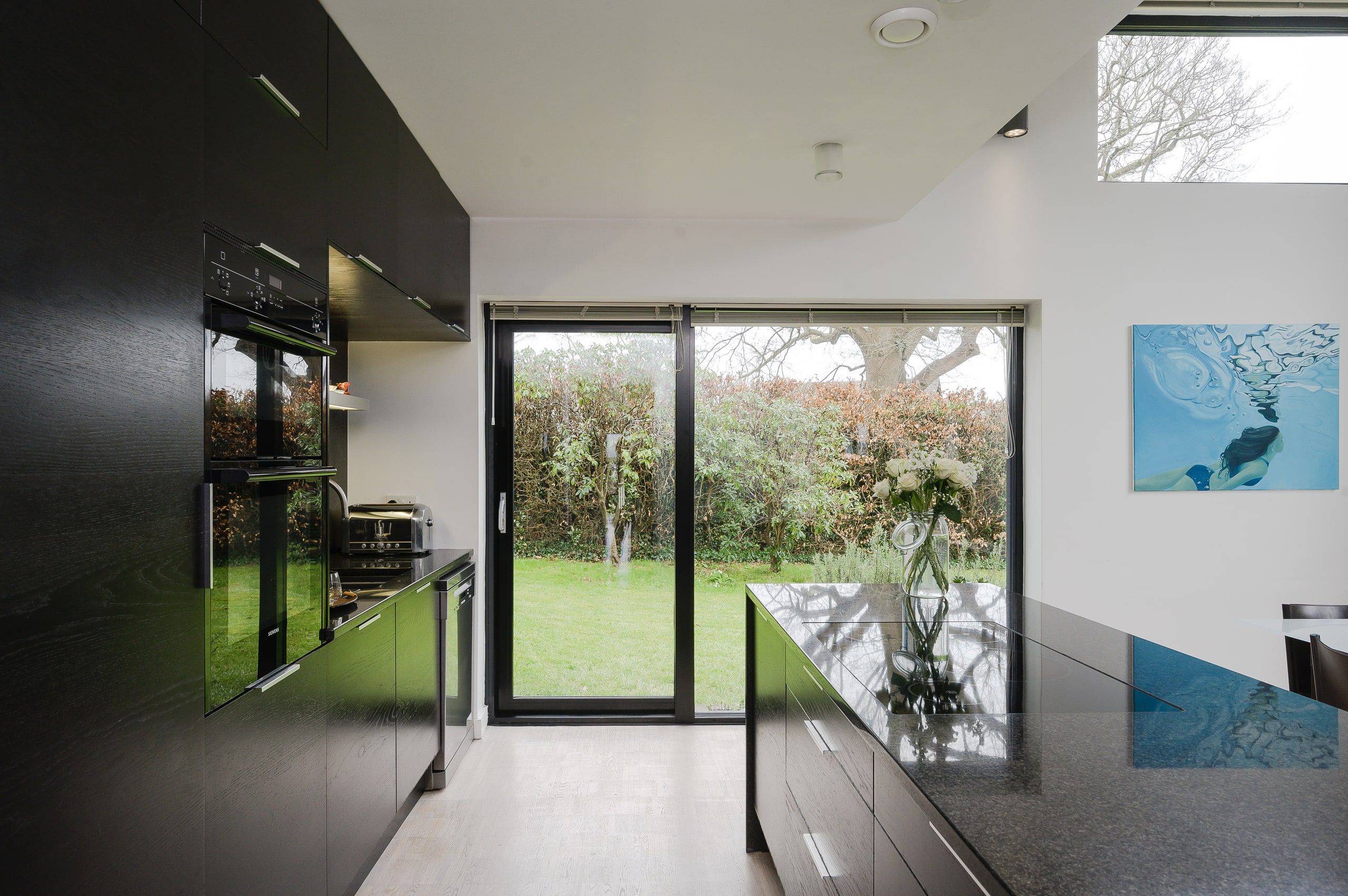 Dark gloss kitchen units and island facing sliding doors onto the lawn, 1960s house, Fernhurst.