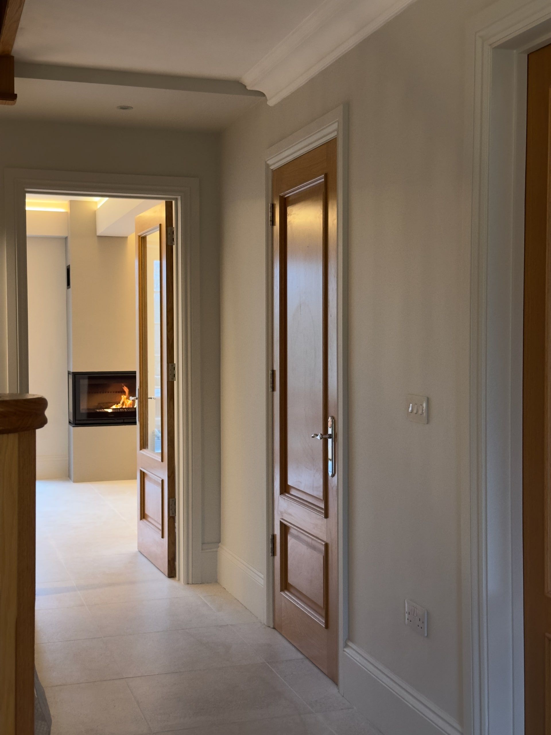 Remodelled entrance hall with the bespoke staircase and a lit fire beyond, detached house, Shackleford.