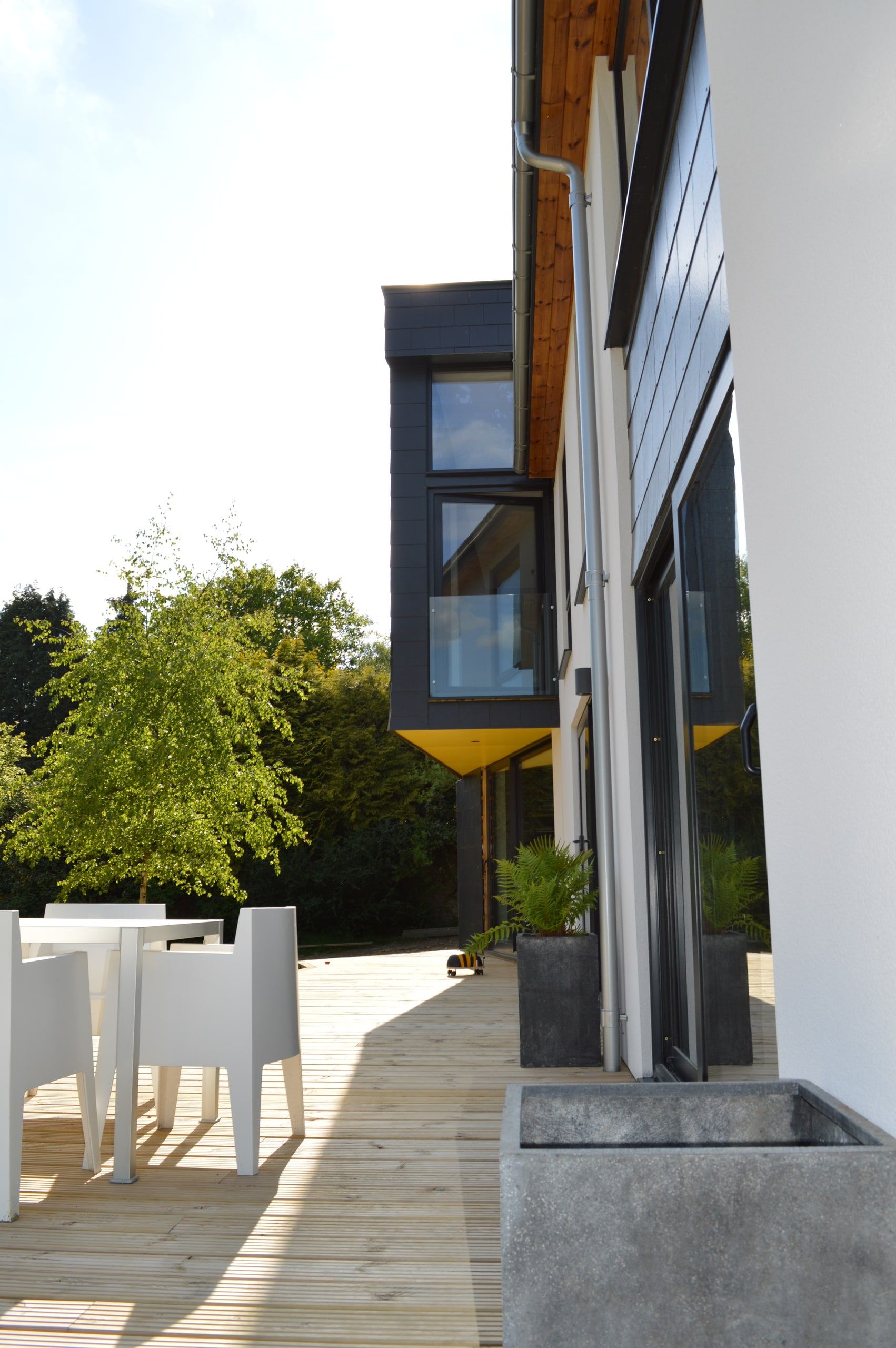 Slate cladding and yellow soffit along the terrace, with ferns in concrete planters, 1960s house, Haslemere.