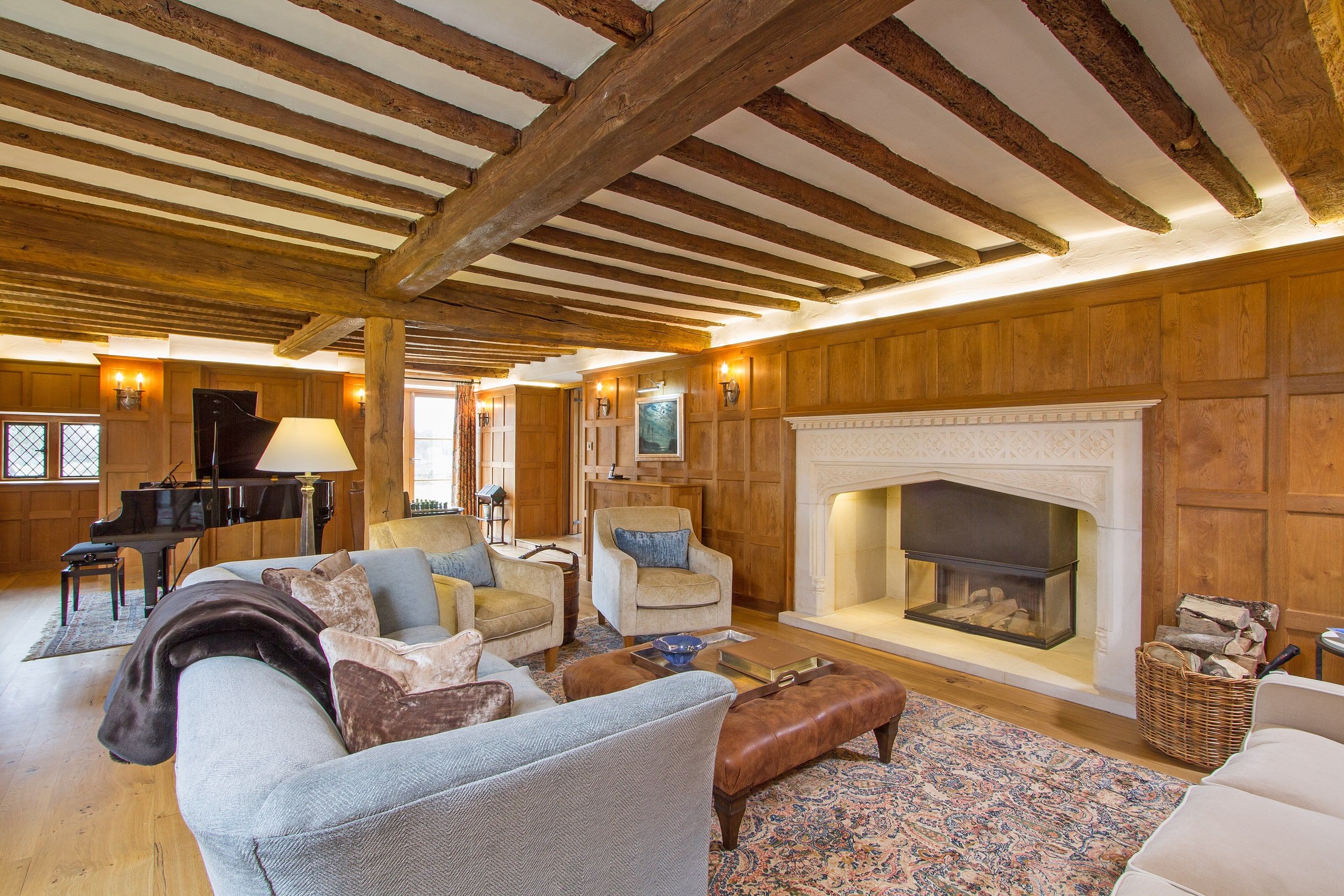 Drawing room with oak panelling, exposed beams and a restored stone fireplace, Grade II listed country house, Chiddingfold.