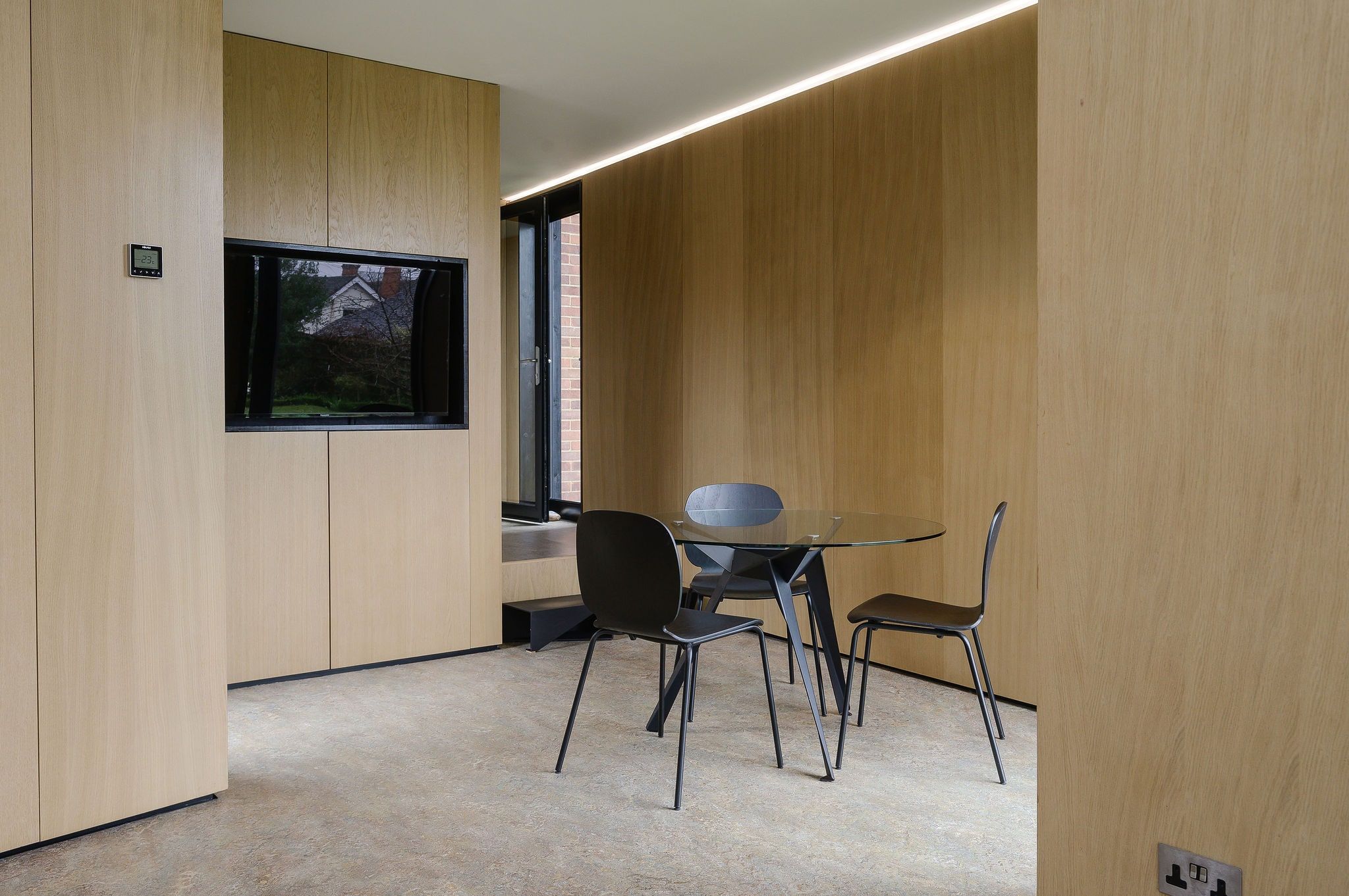 Oak-lined meeting corner with a round glass table and black chairs, ArchitectureLIVE studio, Fernhurst