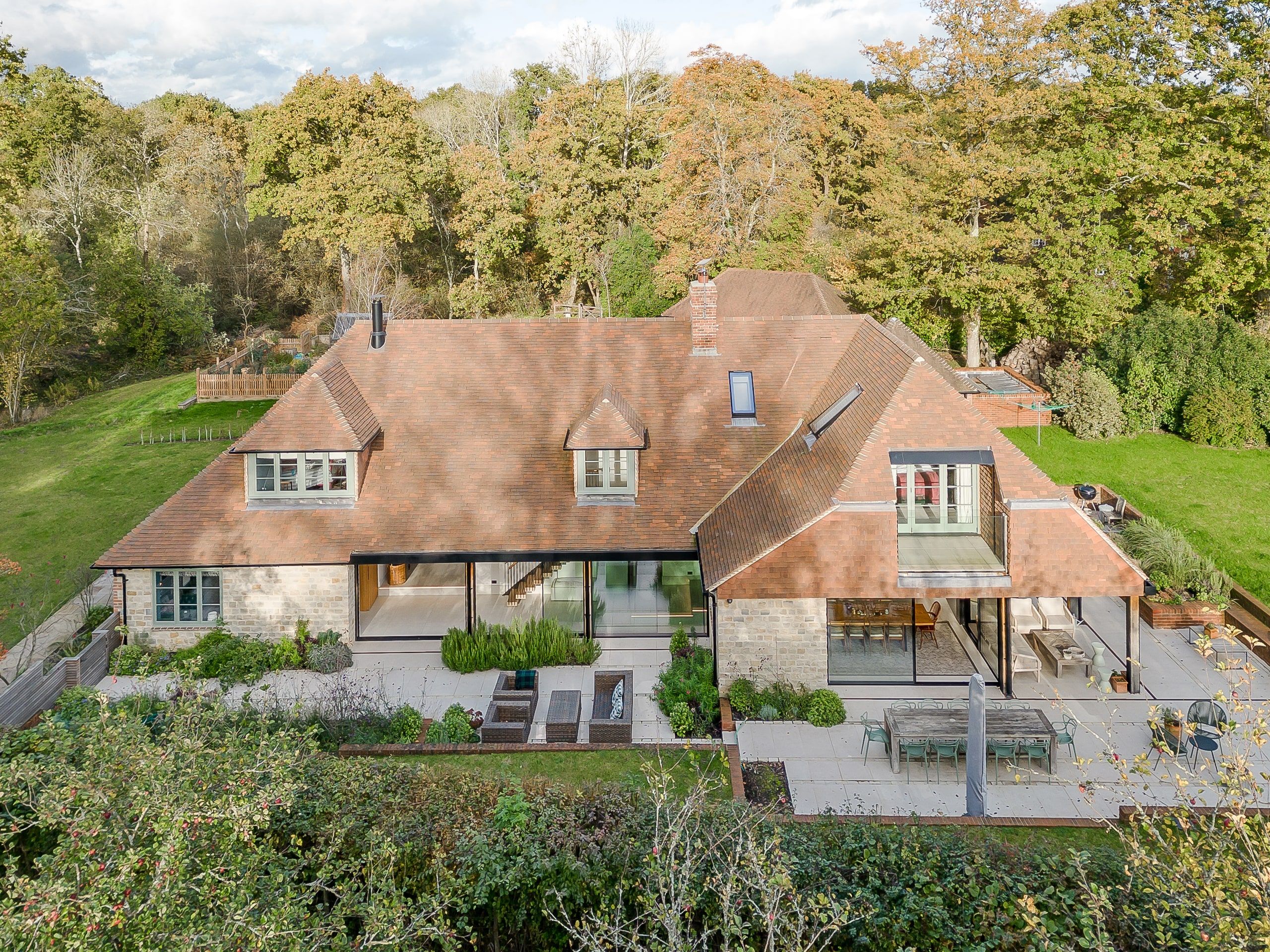 Aerial view of the tiled roofscape and garden terraces set against woodland, country house, Lodsworth