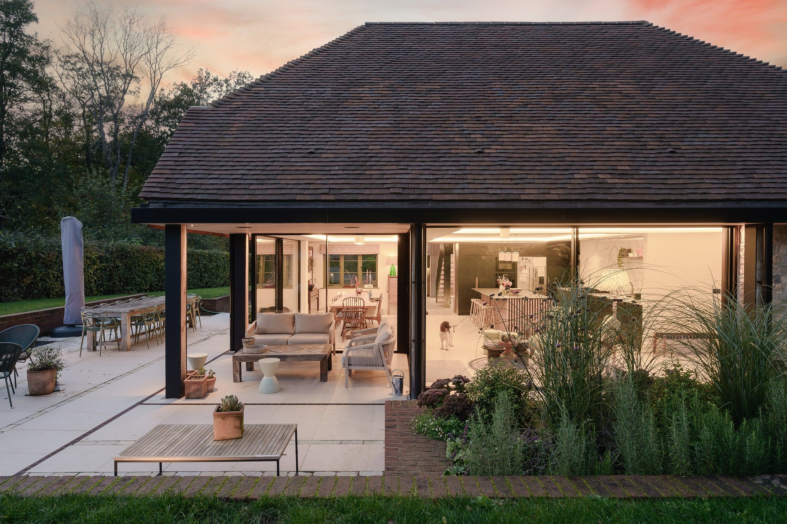 Pink sunset over the loggia, with the open-plan kitchen and living room lit behind, country house, Lodsworth