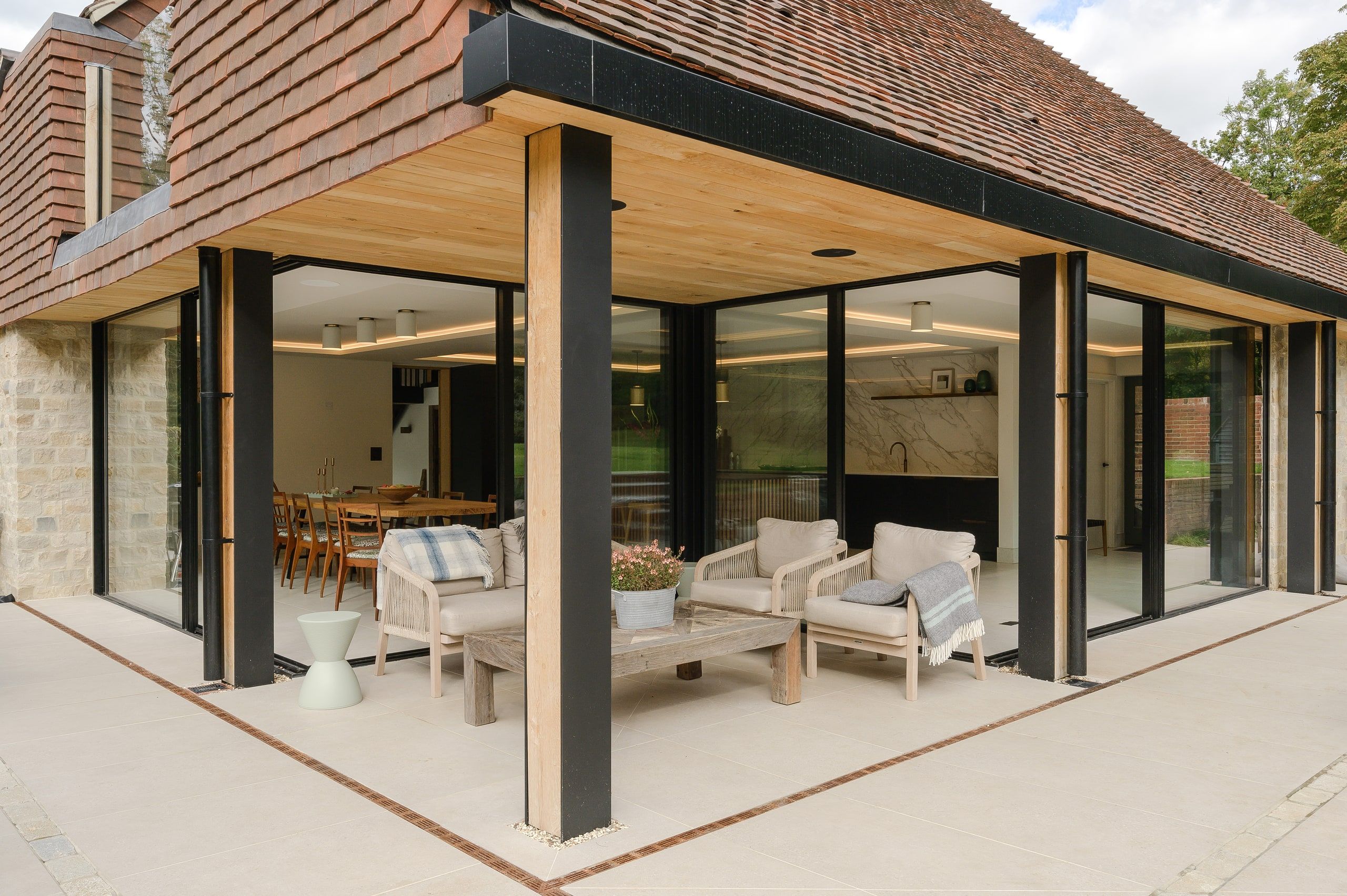 Oak-lined loggia with black steel posts, outdoor seating and the dining room beyond, country house, Lodsworth
