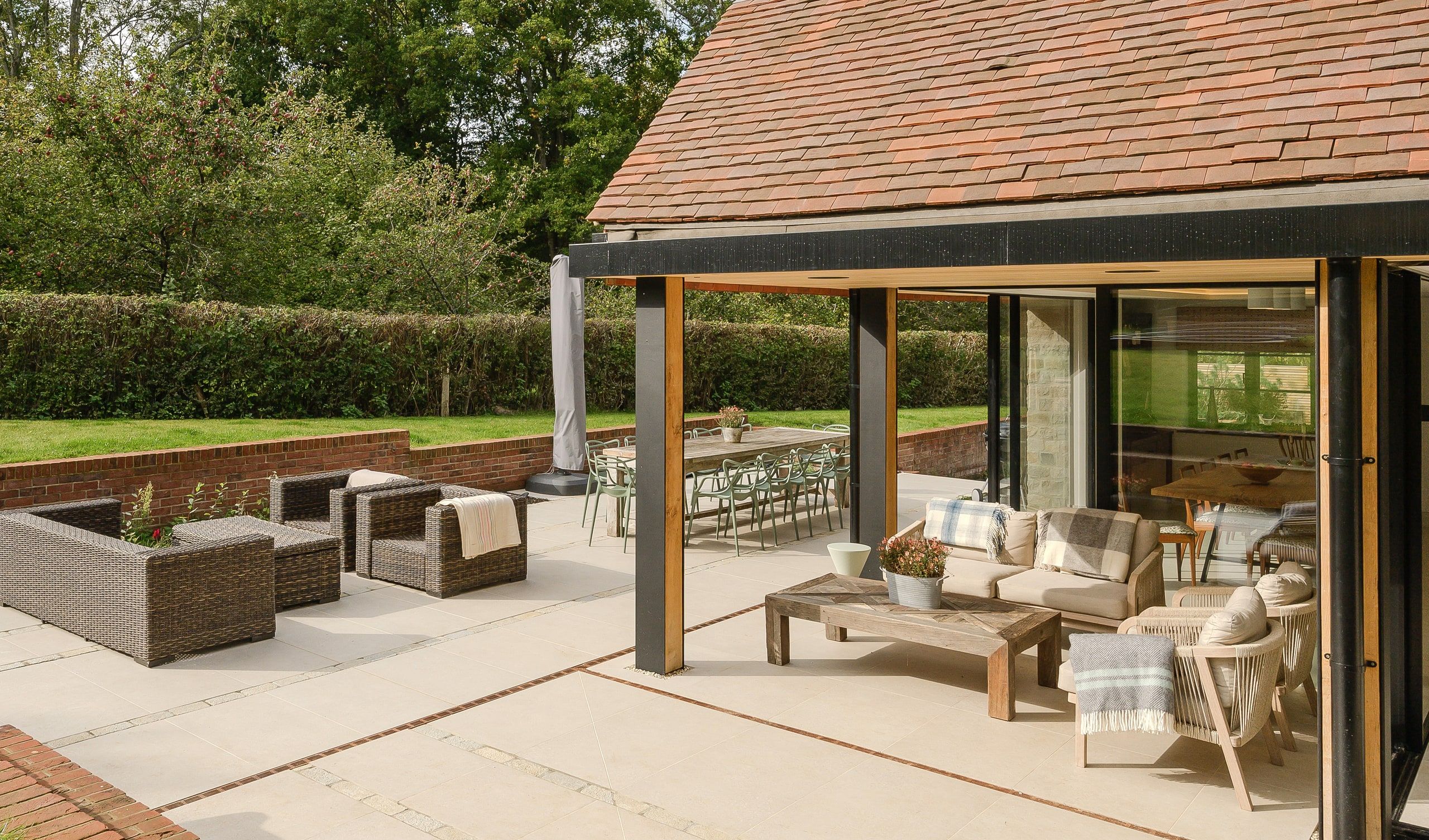 Terrace seating under the loggia, looking back past the long dining table to the hedge, country house, Lodsworth